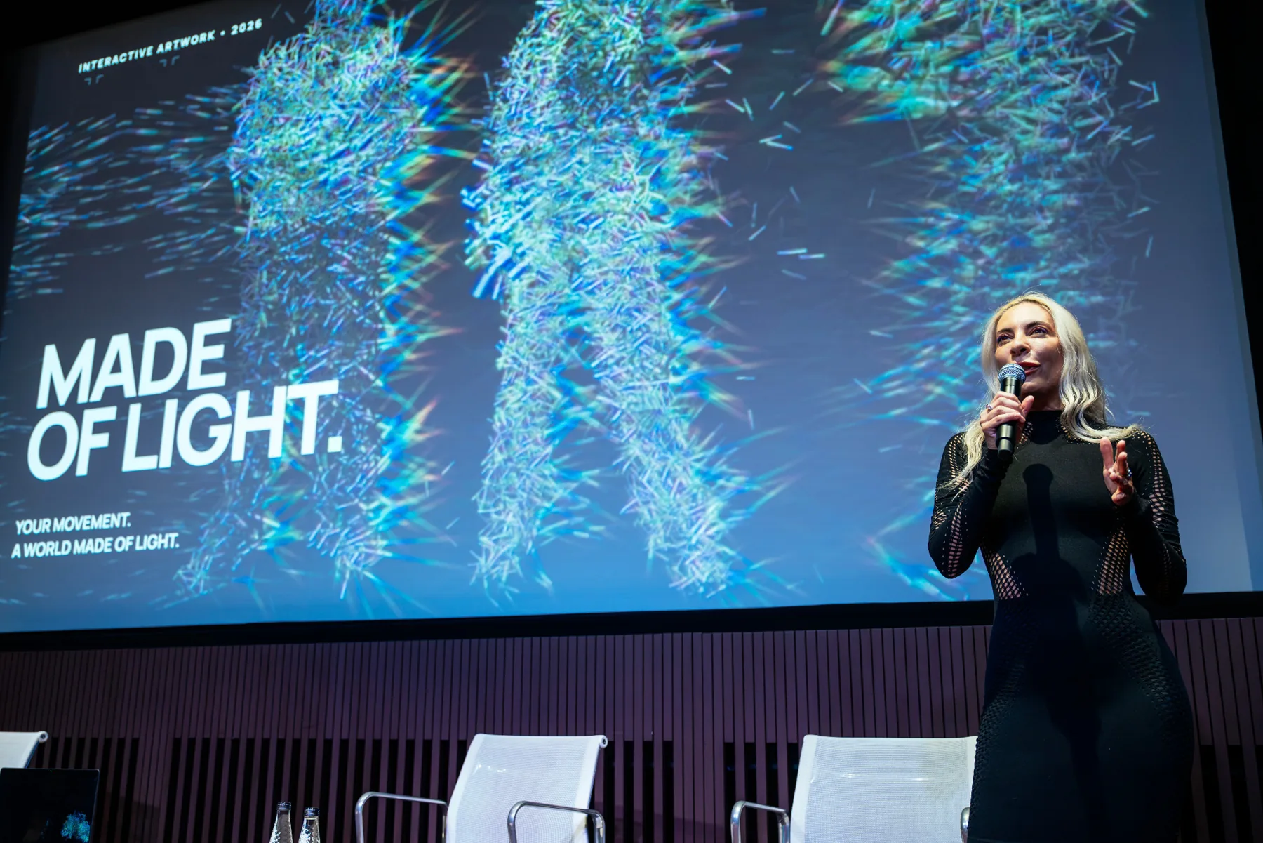 Francesca Rosella speaking on stage at Tate Modern in front of the Made of Light projection